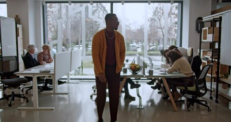 Black male worker enjoying a fun dance moment amidst a busy corporate office setting with team members working in the background.