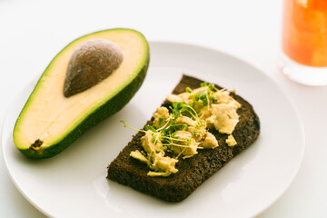 Slice or toast of rye bread on a plate with guacomole with microgreens, half an avocado on a white plate and orange juice on a light background. Healthy, dietary food. Copy space.