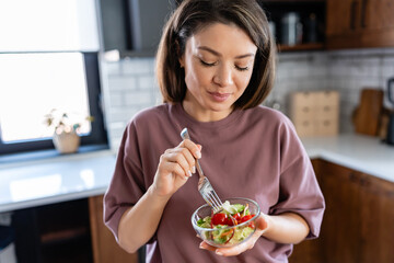 A young pretty cheerful woman is eating a salad. Healthy eating