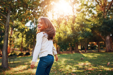 Girl, child and playing in park with leaves for adventure, fun activity or spinning with enjoyment in summer. Kid, happy and excited with freedom, holiday or wellness on grass in nature with sunlight