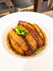 A plate of steamed and braised Pork Belly garnished with green onions, served in a savory sauce, presented on a white plate.