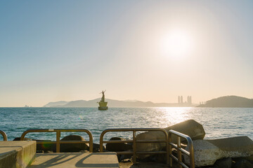a large human figure sculpture on a sea platform, set against a backdrop of mountains under clear skies in Busan, Korea.