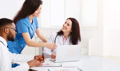 Team Of Practitioners Examining Medical Reports On Laptop, Having Meeting At Hospital