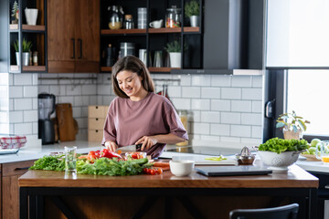 A young pretty cheerful woman is preparing a healthy various vegetable-based meal at home
