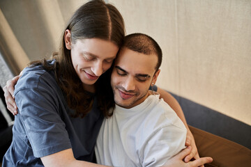 A young gay couple shares a loving embrace inside a modern home.