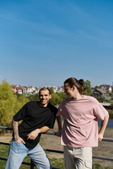 Obraz premium Two young men, dressed casually, stand side-by-side on a railing overlooking a suburban neighborhood on a sunny day.
