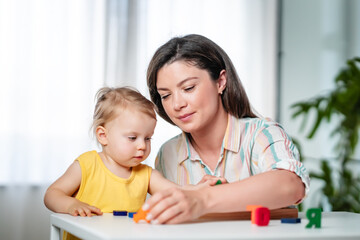 A young mother is playing with her young toddler daughter at home