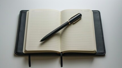 a gray open notebook with a leather cover and a black pen on a light plain background