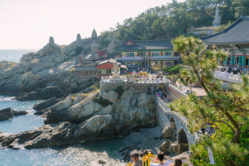 the Haedong Yonggungsa Temple in Busan, Korea, perched on rocky cliffs above the sea with a bridge leading to it under a clear blue sky.