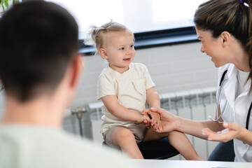 A woman pediatrician is examining her little girl patient and giving advice to her father