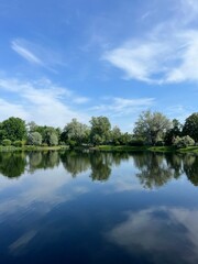 Beautiful tender blue sky reflection on the lake surface, trees silhouettes reflection on the lake surface, summer lake in the park