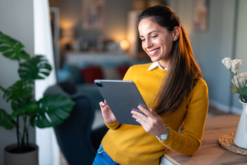 Smiling woman leaning on table at home working on tablet pc. Professional businesswoman looking at...