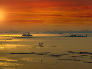 Seascape at golden hour on the horizon, pier and fisherman's farm in the foreground, golden sky and clouds