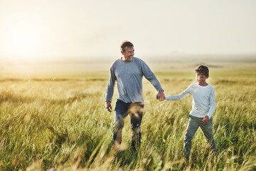 Holding hands, walking and father with kid in nature at sunset for bonding together on vacation. Happy, farm and dad with boy child on adventure, holiday or weekend trip in agriculture countryside.