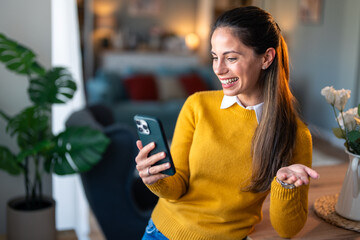 Smiling female entrepreneur discussing over video call on mobile phone while standing in home...