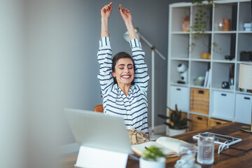 A cheerful Caucasian woman enjoys a moment of success at work, stretching with elation by her...