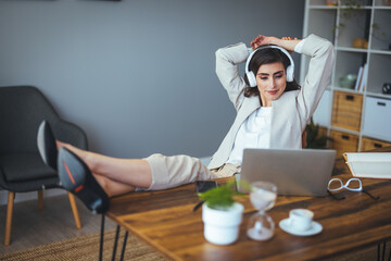 Fototapeta premium A serene Caucasian professional unwinds, feet up, with headphones, in a modern office space while taking a break from work.