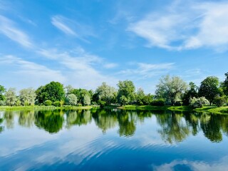 Beautiful tender blue sky reflection on the lake surface, trees silhouettes reflection on the lake surface, summer lake in the park