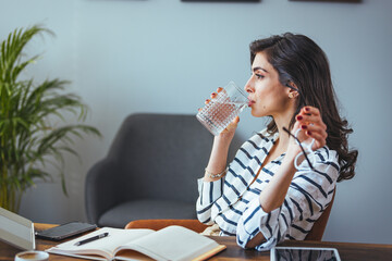 A professional woman sips water in a contemporary office setting, her glance thoughtful, surrounded...
