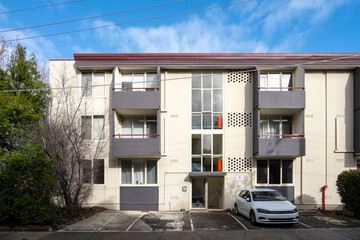 A low-rise walk-up residential apartment building with a staircase and outdoor designated parking for residents.