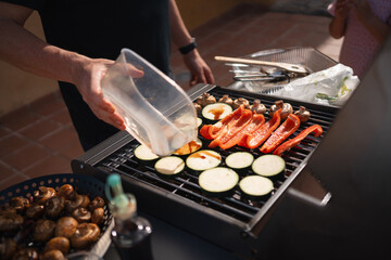 A person pours marinade over vegetables on the grill, preparing them for cooking