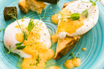 Poached eggs on bread toast with hollandaise sauce and pea greens on a blue plate. Purchase Plan, Selected Focus.