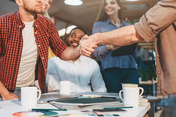 A diverse group of individuals shaking hands over a wooden table during a meeting or negotiation.