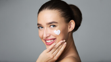 Beauty Skin Care. Cream In Heart Shape On Female Cheek, Grey Studio Background