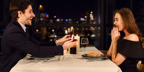 Man making propose with ring to his surprised girlfriend while have date in fancy restaurant. Do you marry me concept.