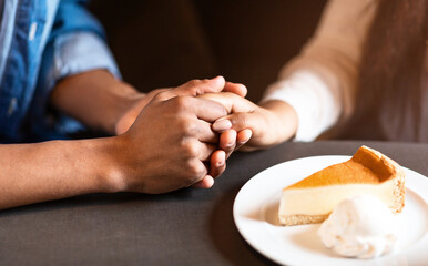 Two individuals are pictured holding hands at a table in a cozy cafe. A slice of cheesecake on a plate with a dollop of whipped cream is in front of them, suggesting a warm and intimate moment