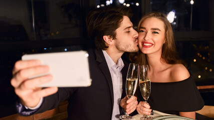 Portrait of kissing couple making selfie photo with smart phone during romantic dinner in restaurant