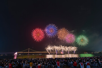 Dazzling fireworks illuminate Busan's night sky, with Gwangan Bridge silhouetted in the background.