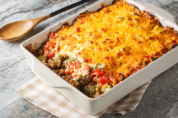 Classic John Wayne casserole has wonderfully southwest flavors, ground beef, a biscuit crust, fresh tomatoes, and a cheesy creamy topping closeup on the baking dish on the table. Horizontal