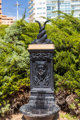 Obraz premium Valencia, Spain - April 20, 2024, A drinking fountain in a park made of black metal in the form of a satyr releasing a stream of water from his mouth.