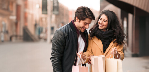 A man and woman are standing on a busy city street, holding shopping bags.