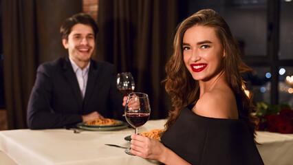 Beautiful young couple wearing nice outfits in a restaurant having romantic evening dating, drinking wine.