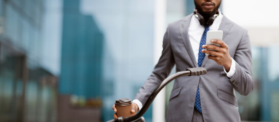An African American businessman is checking his phone while sitting on a bicycle in an urban area. The mood is dynamic and modern, set against a backdrop of city buildings, cropped
