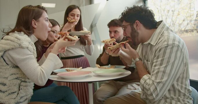 During a relaxed lunch break in a bright office setting, a group of diverse colleagues is seen sharing slices of pizza, fostering a friendly and inclusive work culture.