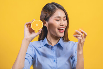 Smiling portrait young woman eating orange isolated on yellow background, half fruit.