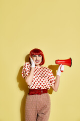 Redhead in polka dot shirt amplifying message with red and white megaphone on yellow backdrop.