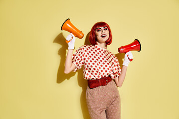 A redhead woman with pop art makeup holds two vibrant megaphones against a yellow background.