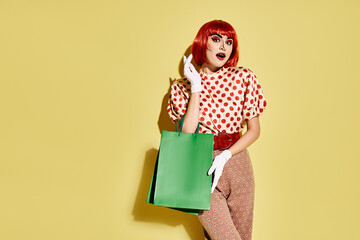 A pretty redhead woman with creative pop art makeup holding a green shopping bag. She wears a polka dot blouse on a yellow background.