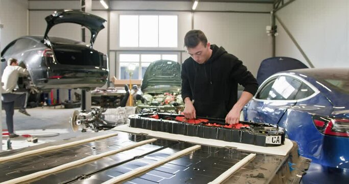 Male technician working on repairing a high-voltage battery pack for an electric vehicle in a modern car repair workshop. Technician Repairing Electric Car Battery in Workshop. Electric car.