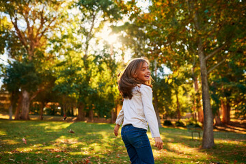 Girl, child and happy in park with leaves for adventure, fun activity or spinning with enjoyment in summer. Kid, playing and excited with freedom, holiday or wellness on grass in nature with mockup