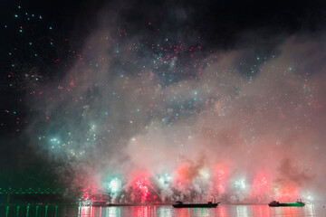 a vibrant fireworks display over a body of water in Busan, Korea, with spectators and a bridge in the background.
