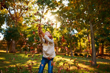 Girl, child and leaves or catch in park for adventure, fun activity and autumn game with enjoyment outdoor. Kid, happy and excited with freedom, holiday or wellness on grass in nature with sunlight