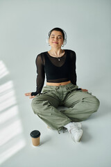 A young woman with short hair sits, exuding effortless style and contemplation on a grey background.