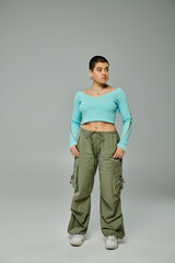 A fashion-forward young woman with short hair strikes a pose in a blue top and cargo pants against...