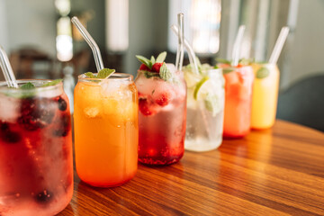 Fruit drinks with berries and ice in glass glasses and straws on a wooden table.
