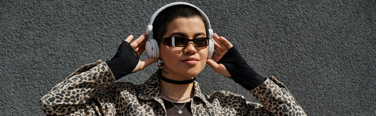 A chic woman wearing sunglasses and a leopard print jacket listens to music through headphones.